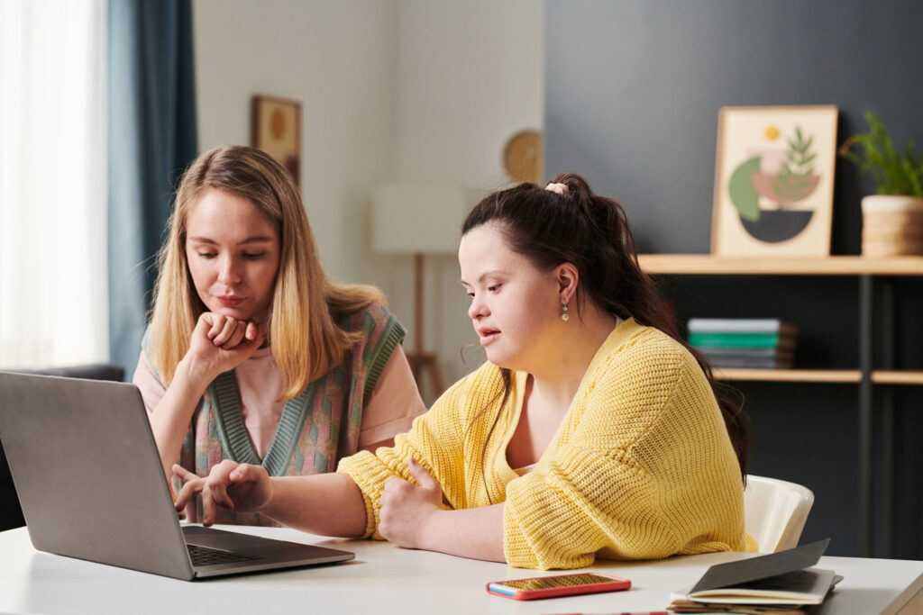 A service provider sits with person served who has Down syndrome in front of laptop