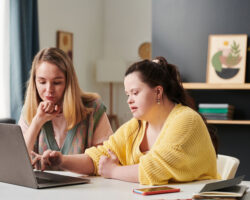 A service provider sits with person served who has Down syndrome in front of laptop