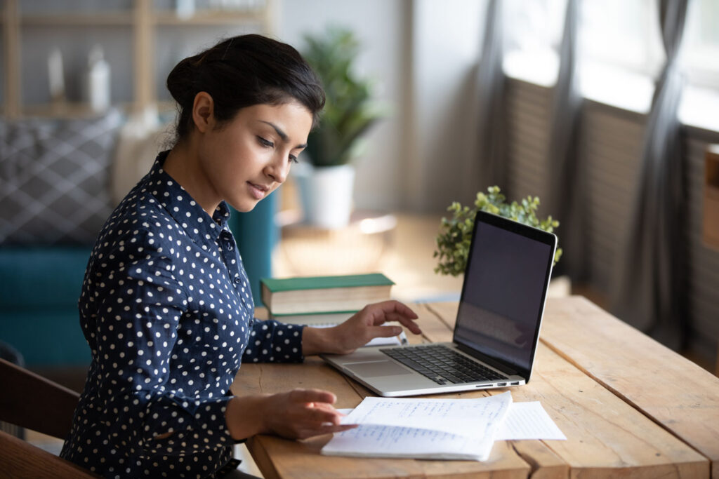 Young female Service Provider sitting with her laptop and looking at notes